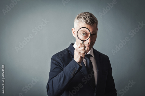 businessman looks at us through a magnifying glass