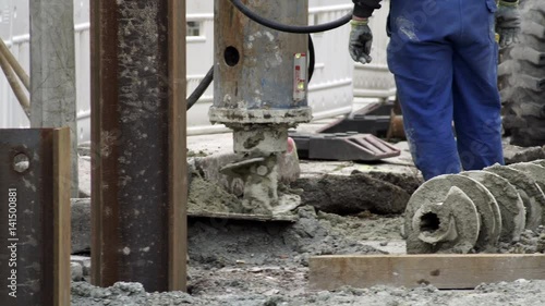 Handheld medium long shot of an industrial post-hole auger drilling head making a hole for pilings on a construction site. photo