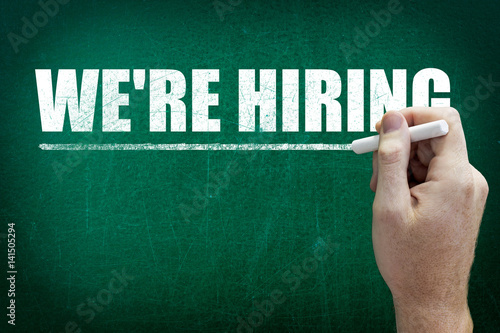 Hand writing the text WE'RE HIRING on the blackboard