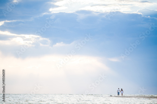 Happy woman and man on honeymoon in beautiful sun light on the beach background. Romantic couple holding hands against the sea. Empty space for the text. Concept of travel.