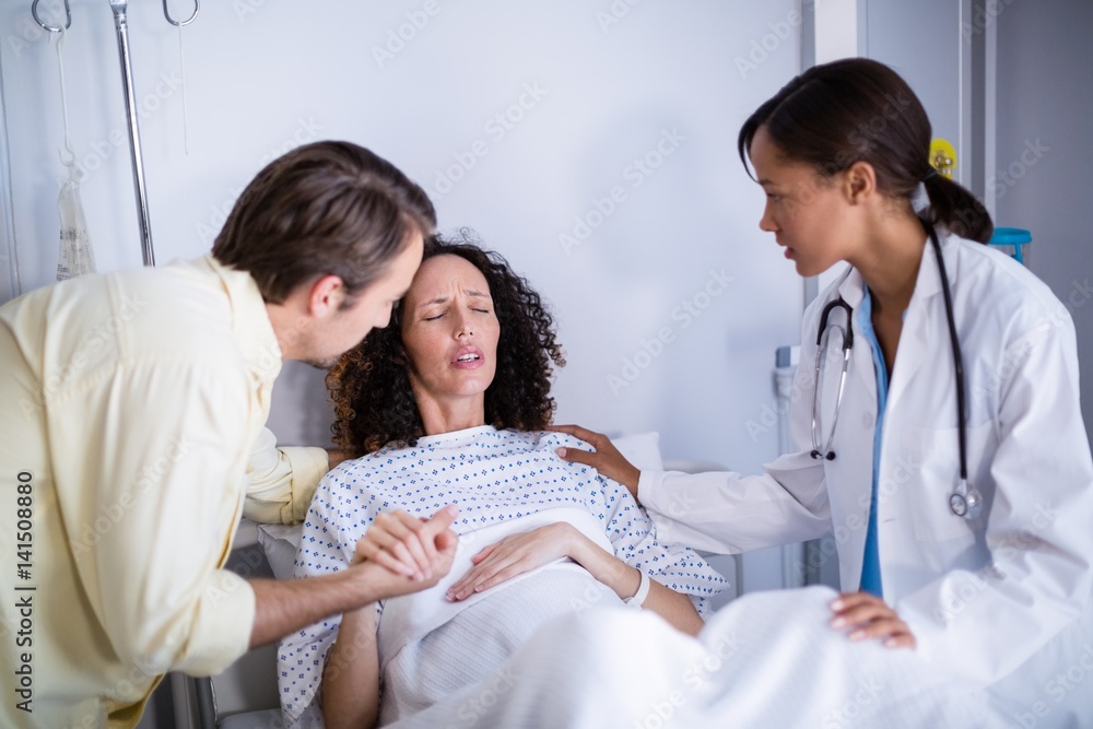 Doctor and man comforting pregnant woman in ward Doctor and man comforting pregnant woman in ward