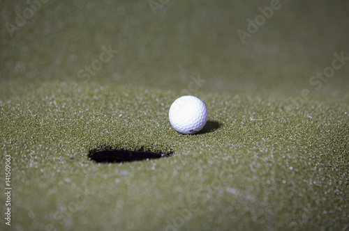 Golf ball next to a hole.