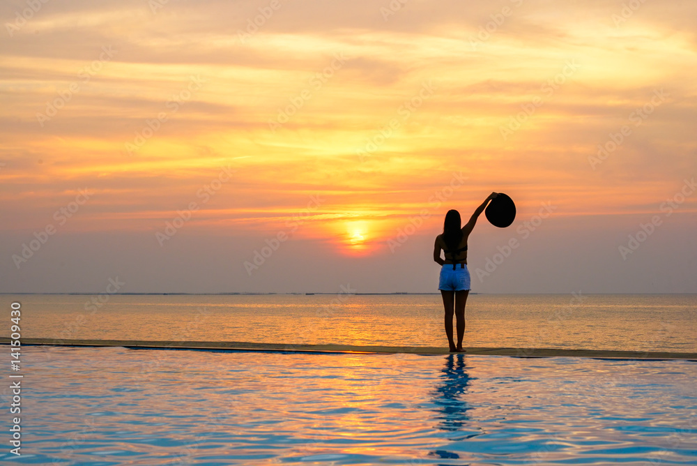 Woman holding hat relaxing at the pool on the sunset and twilight..