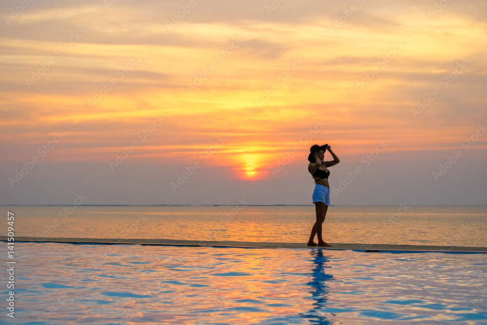 Woman holding hat relaxing at the pool on the sunset and twilight..