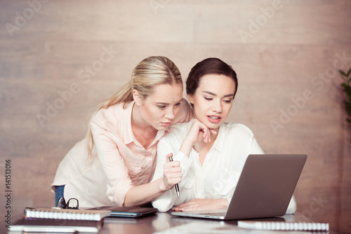 Young concentrated businesswomen looking at laptop photo