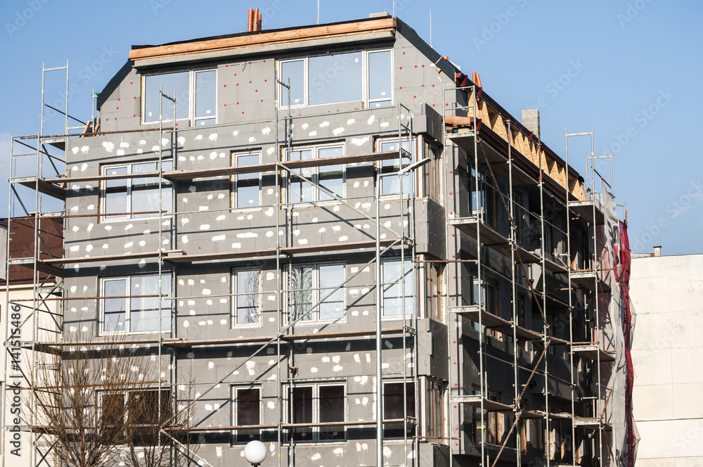 Building under construction with scaffolding for affixing the heat insulation Building under construction with scaffolding for affixing the heat insulation
