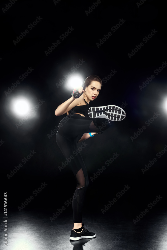 attractive sportswoman training and kicking on black