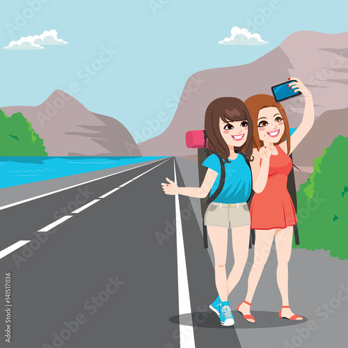 Two young girl friends on travel making selfie with hitchhiking pose on roadside