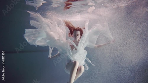 young woman with long red hair swimming underwater like a fairy tale