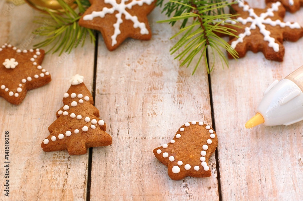 Gingerbread christmas cookies with decorating pen, green pine branch needles with bell and angel on wooden background Gingerbread christmas cookies with decorating pen, green pine branch needles with bell and angel on wooden background