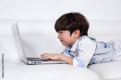 Happy Asian Chinese little boy playing laptop on the couch