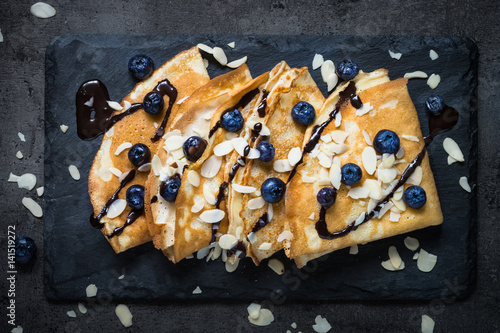 Crepes with blueberries almond flakes and chocolate sauce on black. Top view.