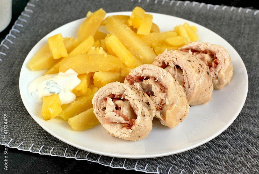 Rolled chicken fillet with prosciuto and mozzarela with pototoes on white plate on grey cloth Rolled chicken fillet with prosciuto and mozzarela with pototoes on white plate on grey cloth