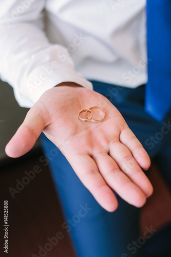 gold wedding rings on the groom's palm in a white shirt, close up. gatherings of the groom on a wedding. wedding concept.