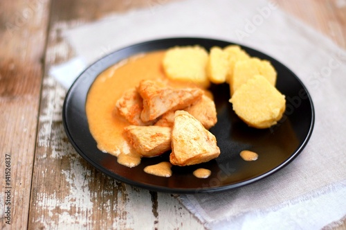 Chicken fillet on sweet pepper with creamy sauce with polenta dumplings on black plate on wooden background