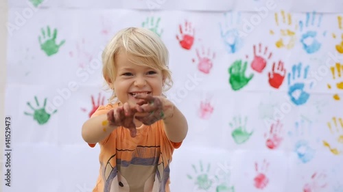 A little happy smiling child scaring by hands in color print on color handprints background in slow motion 50fps