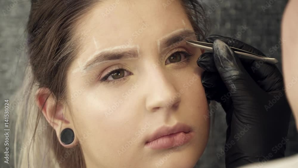 Makeup artist fixing the shape of eyebrows for a woman Makeup artist fixing the shape of eyebrows for a woman