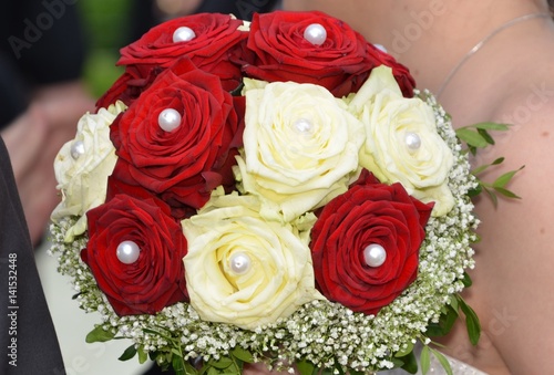 closeup of a wedding bouquet with red and white roses decorated with pearls