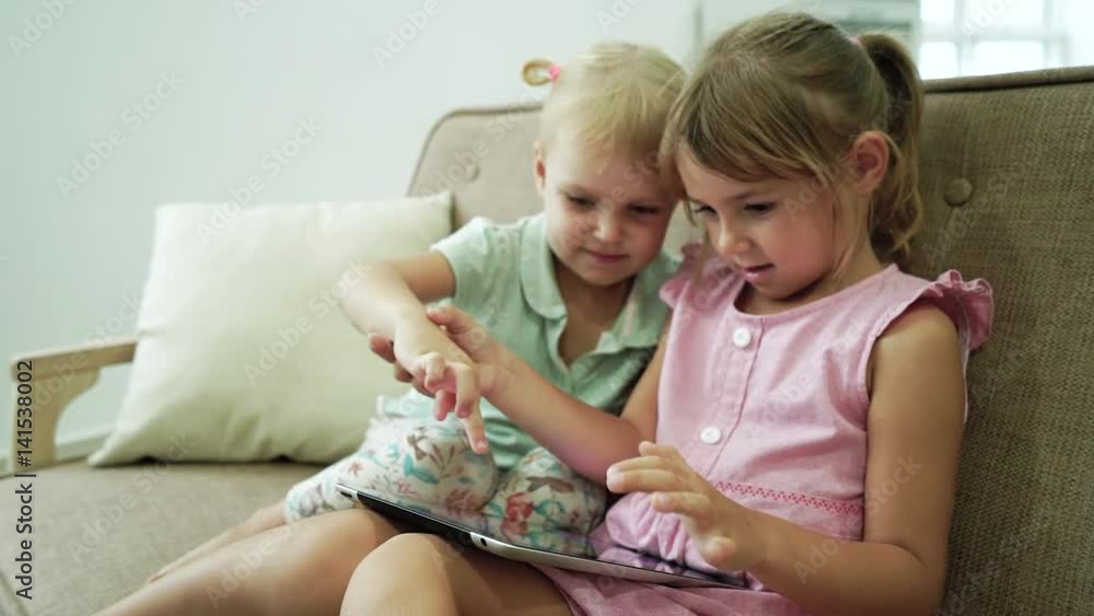 Two little sisters fun playing digital tablet indoor Two little sisters fun playing digital tablet indoor