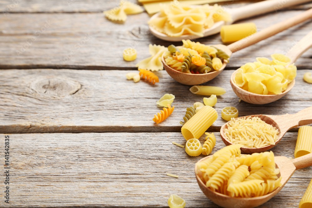 Different kinds of pasta in wooden spoon on grey table Different kinds of pasta in wooden spoon on grey table