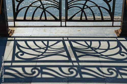 Openwork silhouette and shadow of iron railing on embankment.