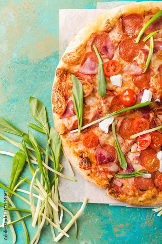 Spring pizza. Salami pizza. Pizza salami on a turquoise abstract background. Copyspace