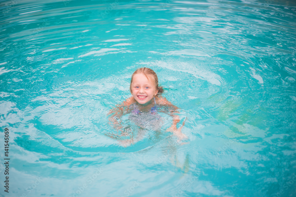 Portrait of cute happy little girl having fun in swimming pool.  Kids sport on family summer vacation. Active healthy holiday
