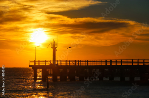 Sunny sunset through pier at the sea