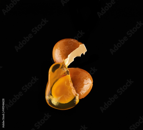 Obraz na plátně Yolk dropping from cracked raw egg divided