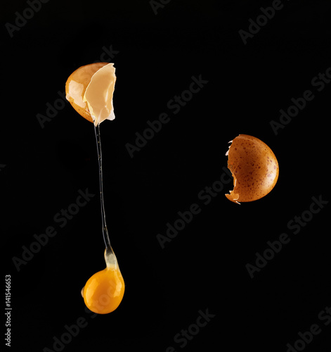Obraz na plátně Yolk dropping from cracked raw egg divided