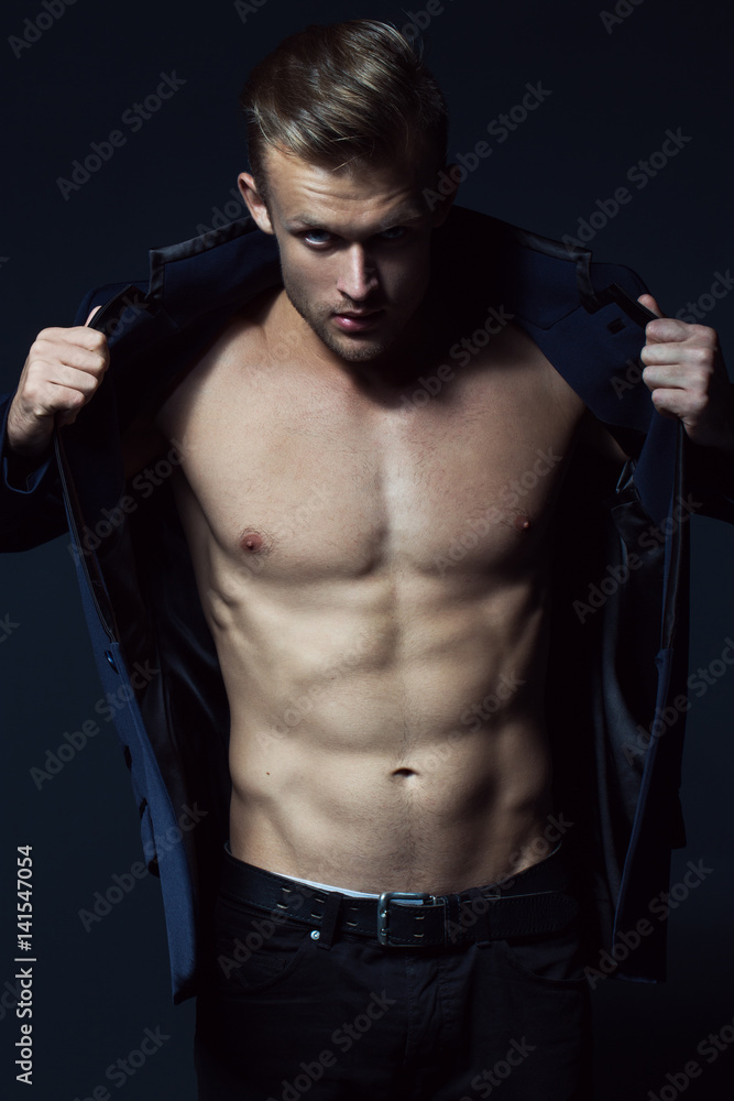 Male beauty concept. Portrait of fashionable young man with stylish haircut wearing jeans and jacket posing over black background. Studio shot