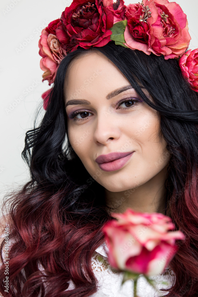 A portrait of a young beautiful woman with red rose flowers on the head. Spring fashion photo