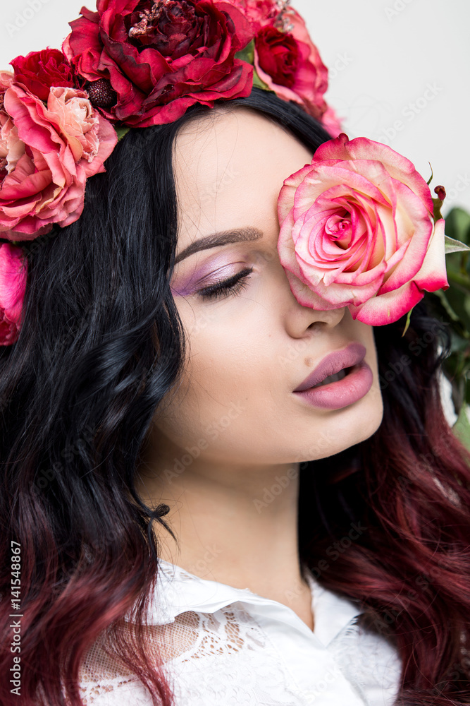 A portrait of a young beautiful woman with red rose flowers on the head. Spring fashion photo