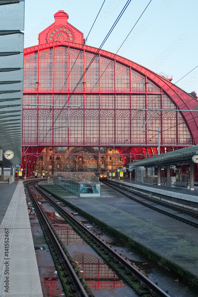 Antwerp Central train station pictured after a rainy day. The monumental red iron building structure is reflected in a puddle.