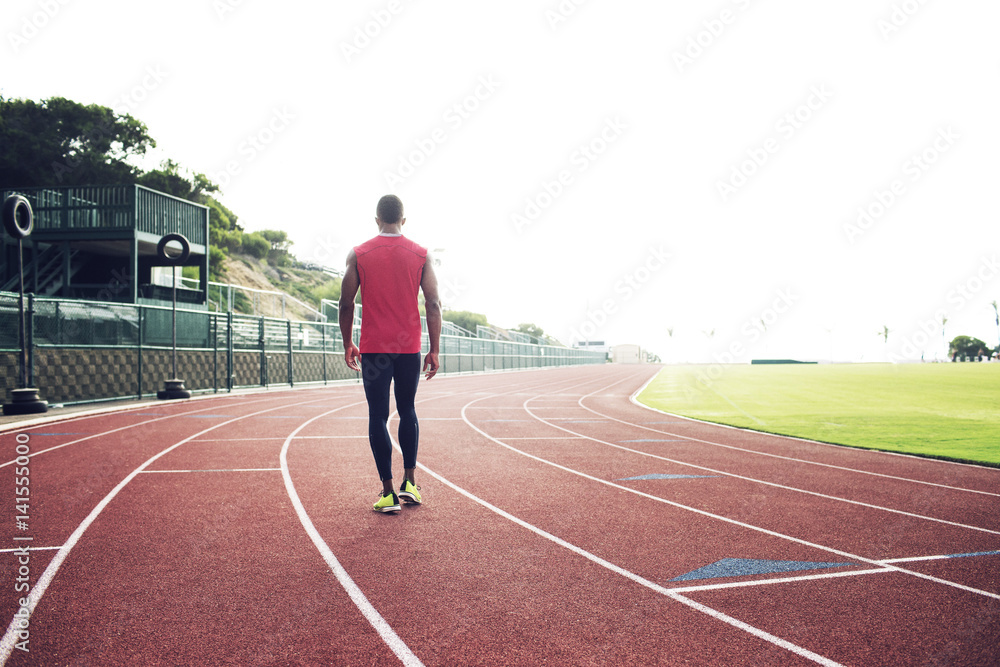 Sportsman walking along running track on stadium Sportsman walking along running track on stadium