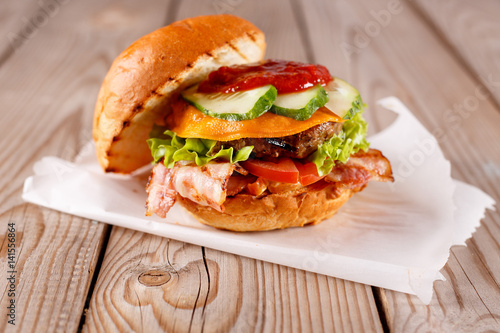 A large open Burger with beef, onions, tomatoes and fried bacon on a wooden table.