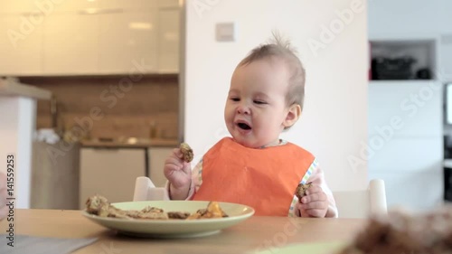 Eleven months old baby girl sitting by the desk, drinking water from the cup; concept of family life and parenting