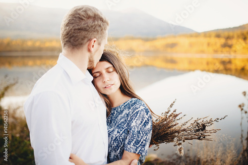 guy and a girl in love embrace each other, kiss, feelings. Against the background of forest and river, sunset, summer and early autumn.