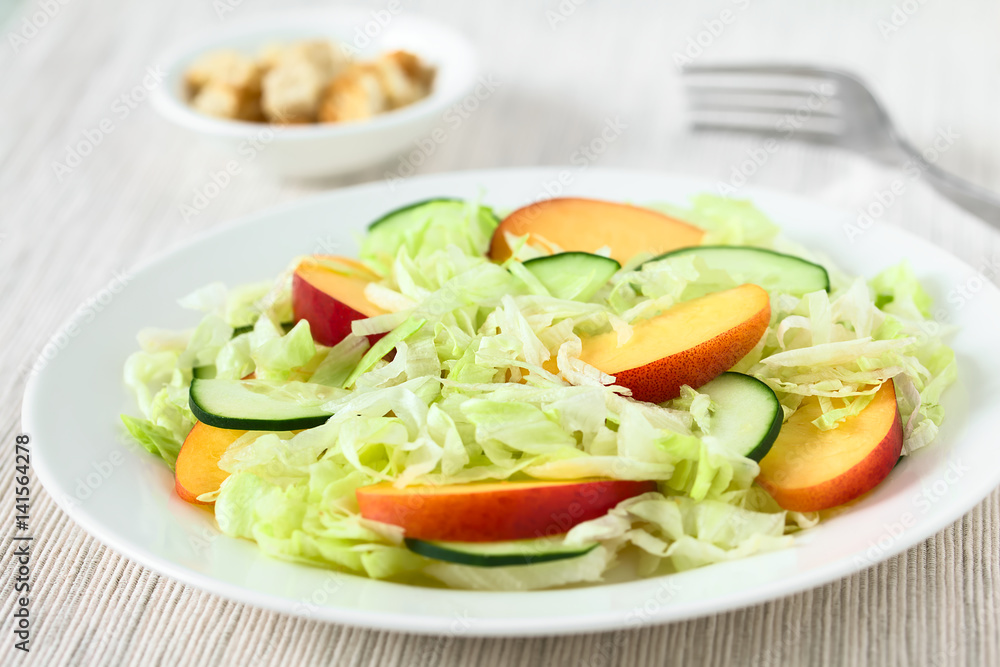 Fresh nectarine, cucumber and iceberg lettuce salad on plate, photographed with natural light (Selective Focus, Focus in the middle of the salad)