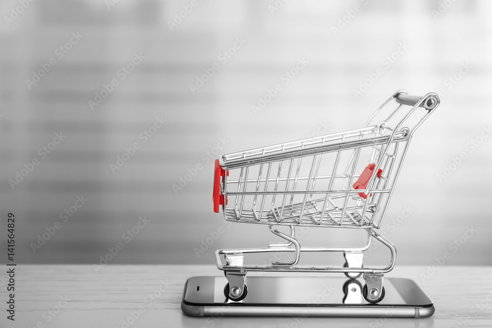 Online shopping concept. Smartphone with mini market trolley on wooden table Online shopping concept. Smartphone with mini market trolley on wooden table