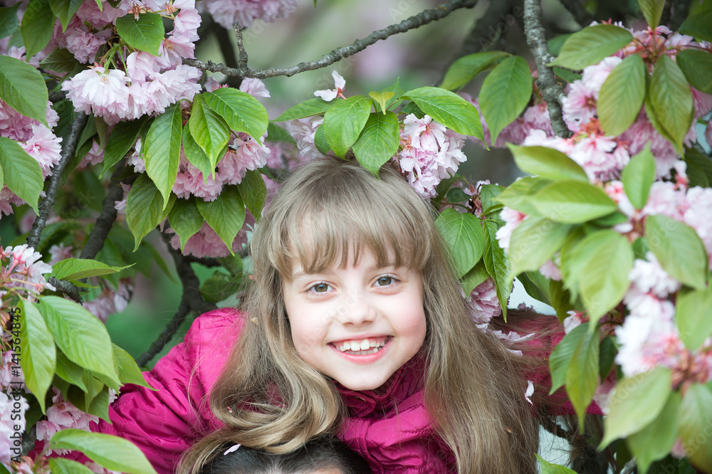 Fototapeta premium small baby girl with smiling face among pink sakura blossom