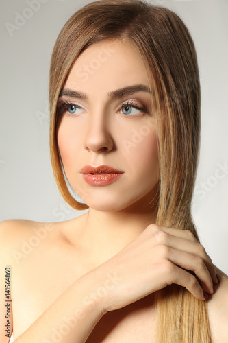 Beautiful young woman with long straight hair on light background