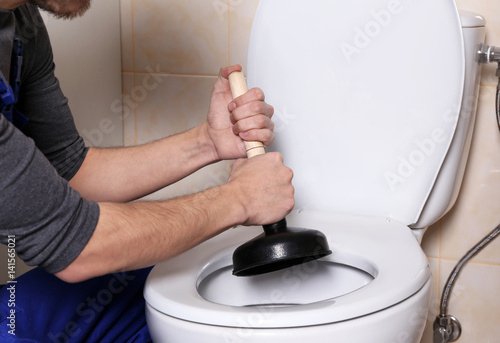 Canvas Print Plumber repairing toilet with hand plunger