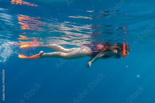 Girl in orange swimming mask and flippers dive in deep sea