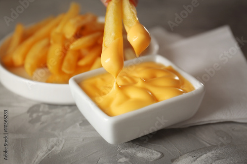 Dipping tasty fries into cheese sauce in bowl, closeup