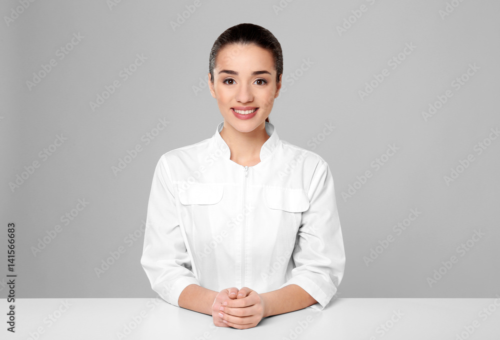Young woman pharmacist standing at table on grey background Young woman pharmacist standing at table on grey background