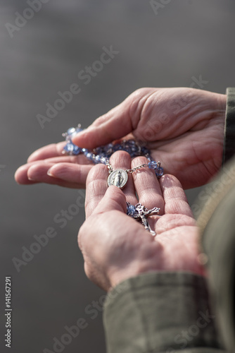 woman holding cross and rosary praying with lake and sun reflection
