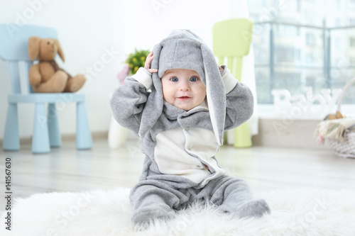 Cute little baby in bunny costume sitting on furry rug at home