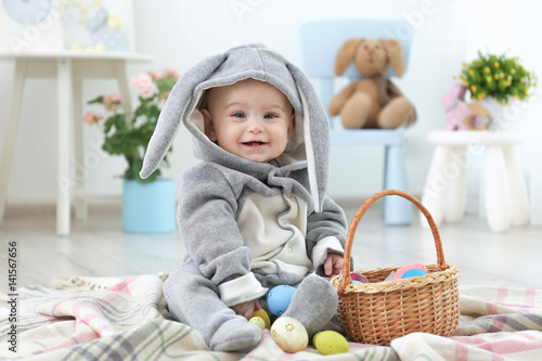 Cute little baby in bunny costume playing with Easter eggs at home
