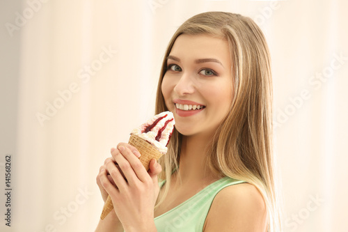 Beautiful young woman with ice cream on light background